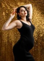 Portret ciążowy w stylu glamour, z przyszłą mamą w lśniącej, złotej sukni, otoczoną luksusowymi akcesoriami, świętującą oczekiwanie na narodziny dziecka